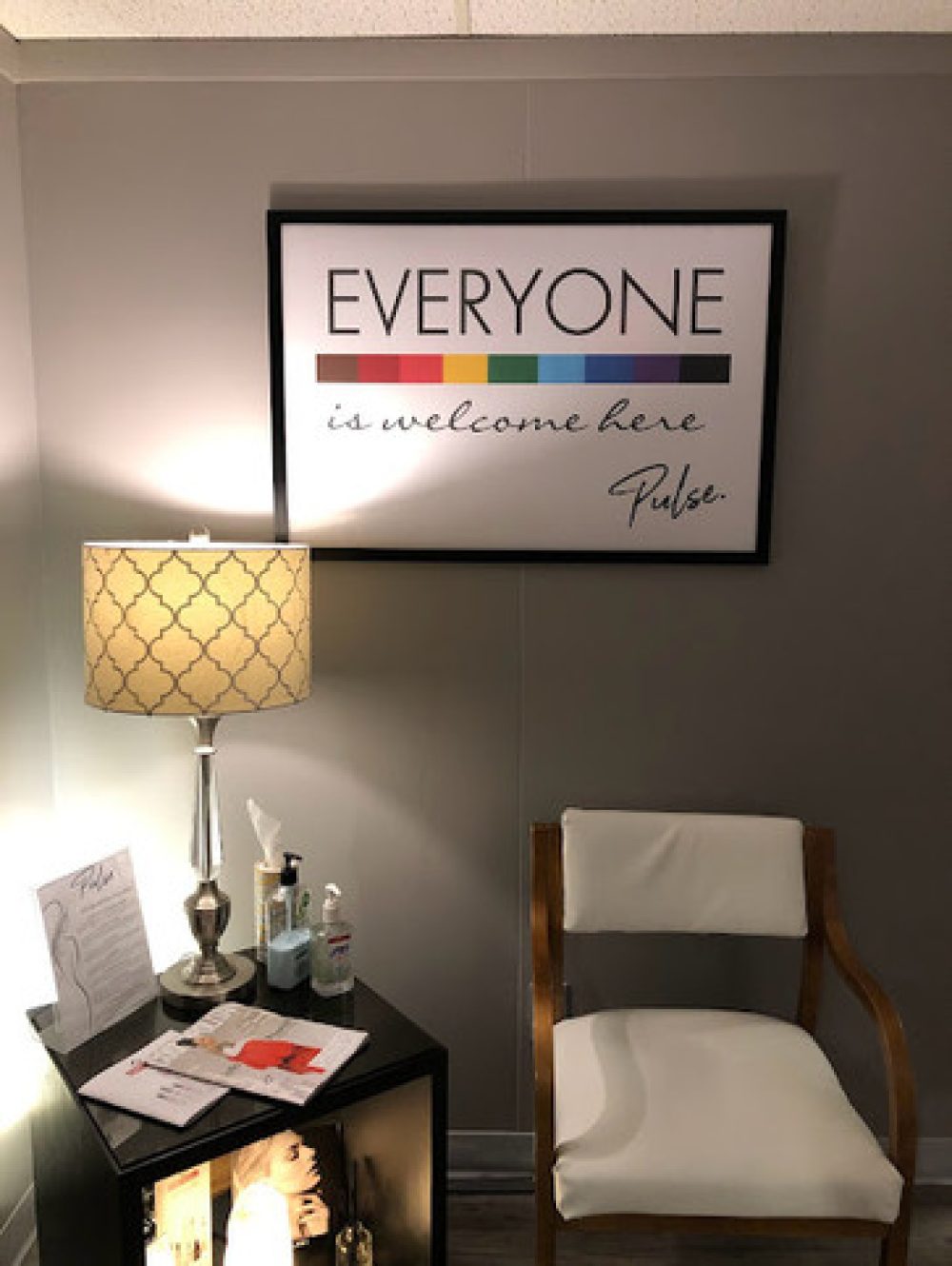 A wooden chair and table with a sign that reads "Everyone Welcome" in a cozy cafe setting.