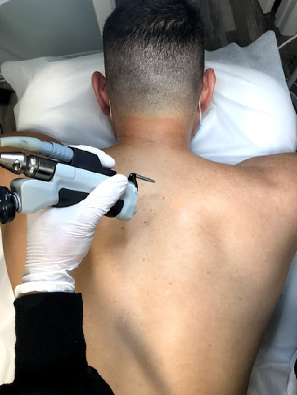 A man sitting in a chair at a tattoo parlor, grimacing as a tattoo artist works on his back.